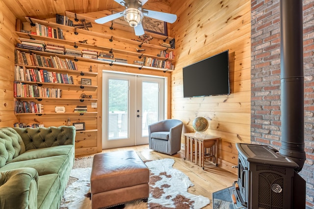 living room with a wood stove, light hardwood / wood-style flooring, wooden walls, and french doors