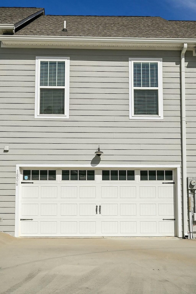 view of side of home featuring an attached garage and roof with shingles