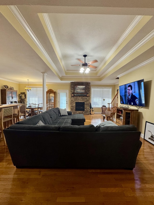 living room with ornamental molding, dark hardwood / wood-style floors, a tray ceiling, a fireplace, and ceiling fan with notable chandelier