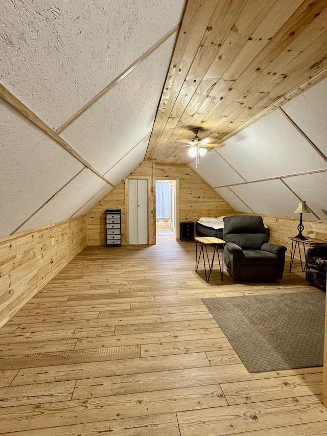 bonus room featuring ceiling fan, lofted ceiling, light hardwood / wood-style floors, and wood walls