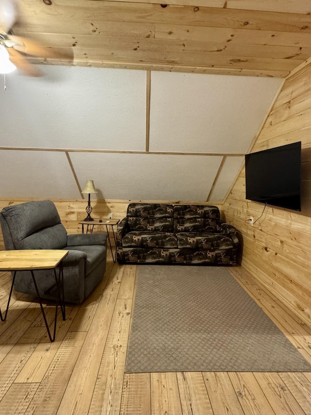 living area with vaulted ceiling, wooden walls, ceiling fan, and light wood-type flooring