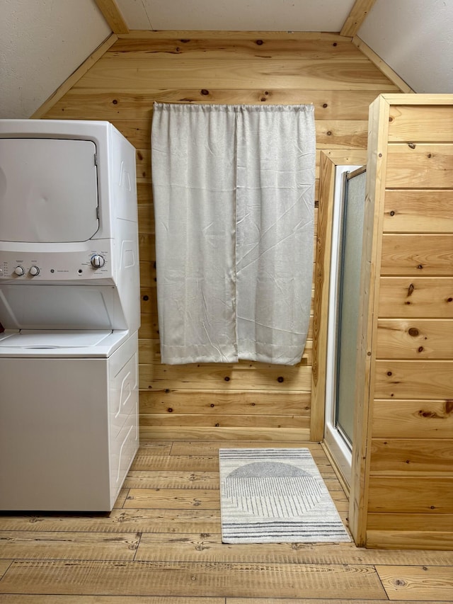 laundry room featuring wooden walls, light hardwood / wood-style floors, and stacked washer and clothes dryer