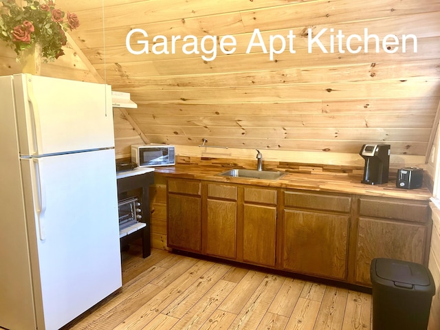 kitchen featuring wooden walls, sink, white fridge, and light hardwood / wood-style flooring