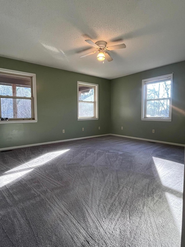 unfurnished room with ceiling fan, dark carpet, a healthy amount of sunlight, and a textured ceiling