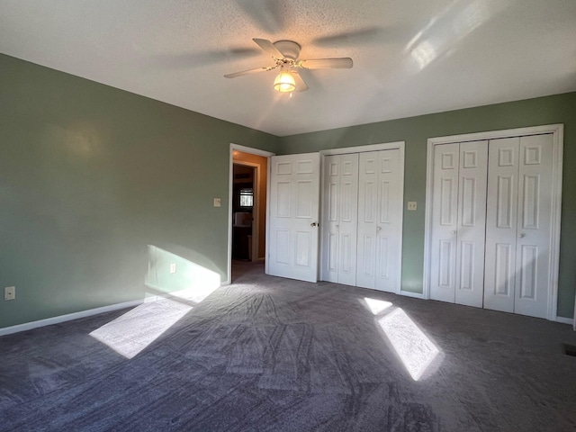 unfurnished bedroom with ceiling fan, two closets, dark carpet, and a textured ceiling