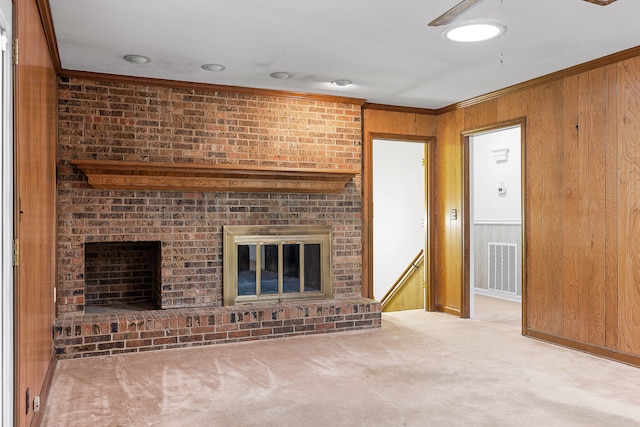 unfurnished living room featuring wooden walls, crown molding, light carpet, and a brick fireplace