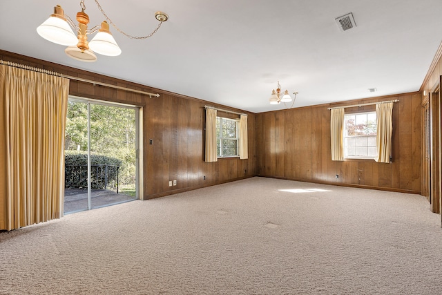 carpeted spare room with a chandelier, a wealth of natural light, and wood walls