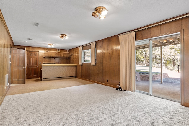 unfurnished living room featuring wood walls, light colored carpet, and a textured ceiling