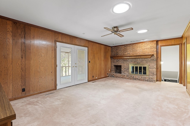 unfurnished living room featuring a fireplace, french doors, ceiling fan, and wood walls