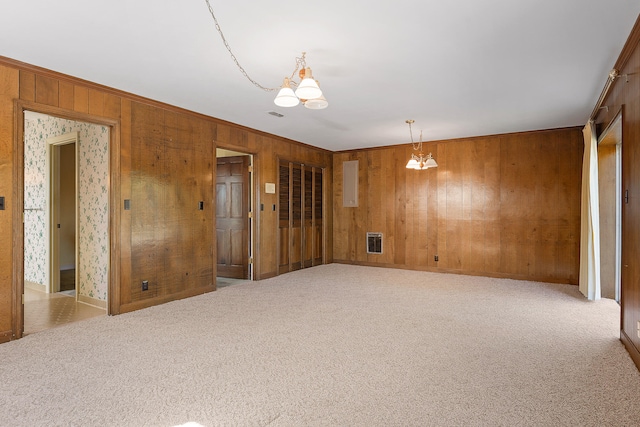 carpeted spare room with a notable chandelier and wood walls