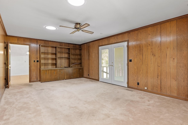 carpeted spare room featuring ceiling fan, french doors, built in features, crown molding, and wooden walls