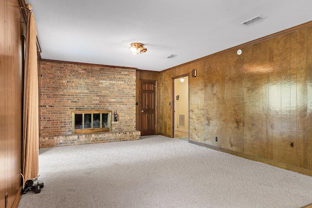 unfurnished living room featuring carpet flooring, wooden walls, ornamental molding, and a brick fireplace