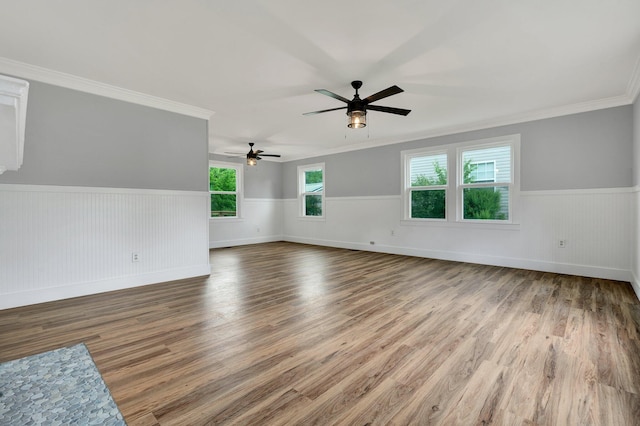 empty room featuring a ceiling fan, wood finished floors, a wainscoted wall, baseboards, and ornamental molding
