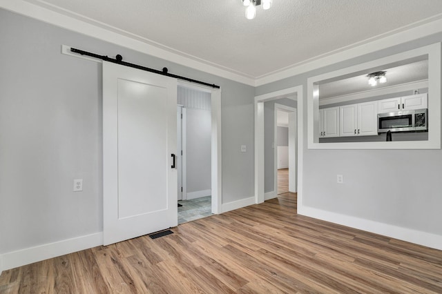 unfurnished living room featuring baseboards, a textured ceiling, light wood-style floors, and a barn door