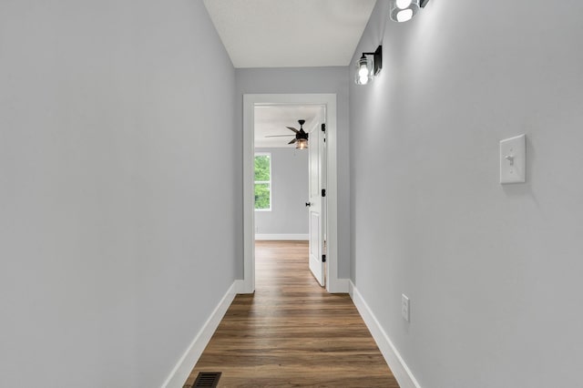 hall featuring dark wood-type flooring, visible vents, and baseboards