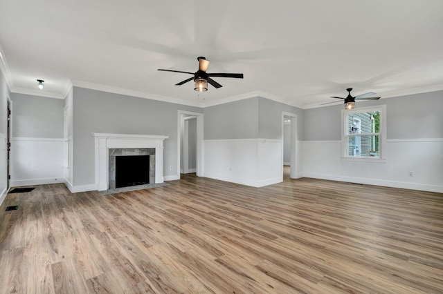 unfurnished living room with a high end fireplace, wood finished floors, visible vents, a ceiling fan, and ornamental molding