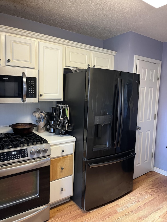 3722 Lockerbie Ln, Powder Springs, GA 30127 - kitchen with light wood-style flooring, light countertops, a textured ceiling, white cabinetry, and appliances with stainless steel finishes