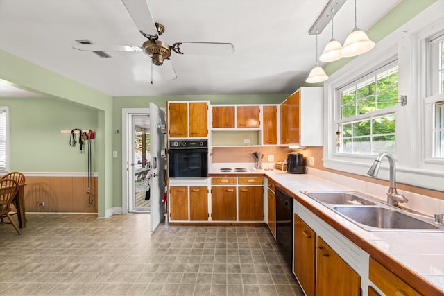 kitchen with tile countertops, black appliances, sink, hanging light fixtures, and ceiling fan