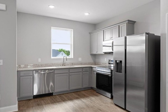 kitchen with appliances with stainless steel finishes, sink, hardwood / wood-style flooring, light stone countertops, and gray cabinets