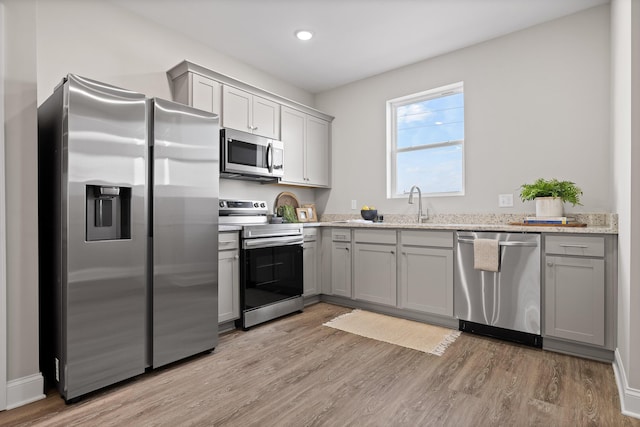 kitchen with light wood-type flooring, appliances with stainless steel finishes, gray cabinets, and light stone counters