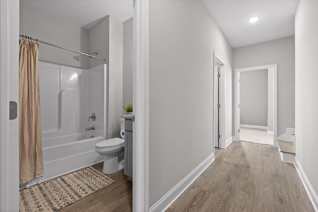 bathroom featuring toilet, wood finished floors, vanity, baseboards, and shower / bathtub combination with curtain