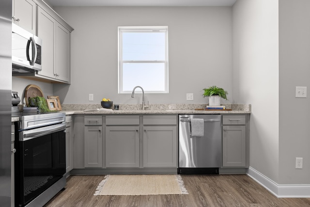 kitchen with gray cabinetry, stainless steel appliances, a sink, baseboards, and dark wood finished floors