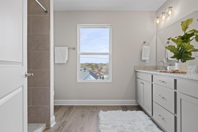 bathroom featuring baseboards, tiled shower, wood finished floors, and vanity