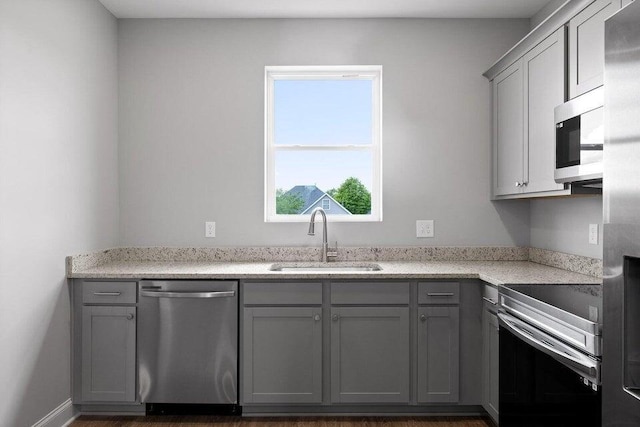 kitchen featuring light stone countertops, sink, appliances with stainless steel finishes, and gray cabinetry