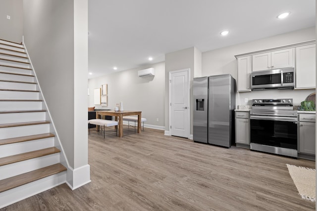 kitchen featuring recessed lighting, appliances with stainless steel finishes, a wall mounted AC, light wood-type flooring, and gray cabinets