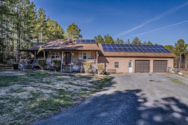 view of front of home featuring covered porch, solar panels, an attached garage, and driveway