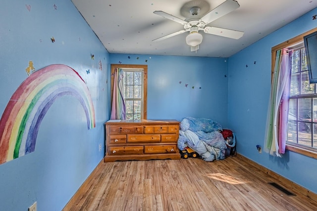 unfurnished bedroom with ceiling fan, multiple windows, wood finished floors, and visible vents