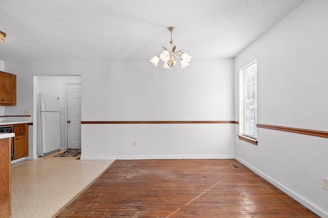 unfurnished dining area with wood-type flooring, a notable chandelier, and a textured ceiling