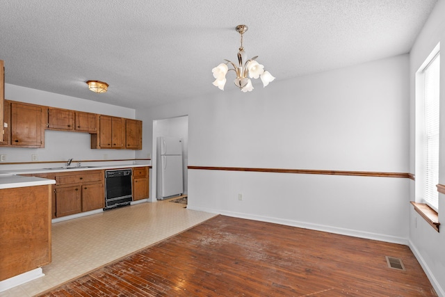 kitchen with decorative light fixtures, black dishwasher, white refrigerator, an inviting chandelier, and sink