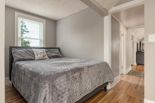 bedroom featuring hardwood / wood-style flooring, vaulted ceiling, and a textured ceiling