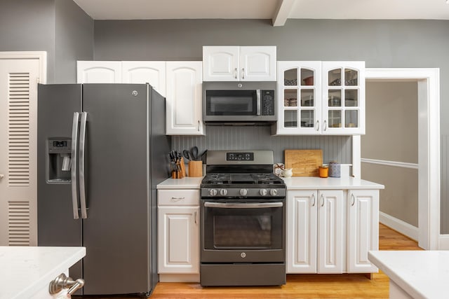 kitchen with white cabinetry, beam ceiling, light wood-type flooring, and appliances with stainless steel finishes