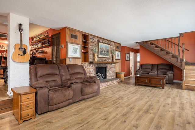 living room featuring built in features, a textured ceiling, light wood-type flooring, and a fireplace