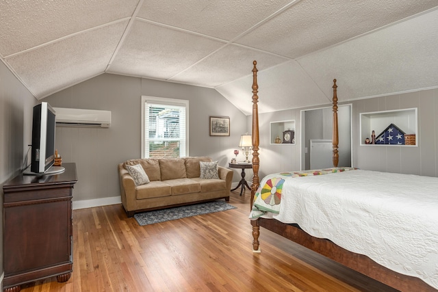 bedroom featuring an AC wall unit, hardwood / wood-style floors, lofted ceiling, and a textured ceiling