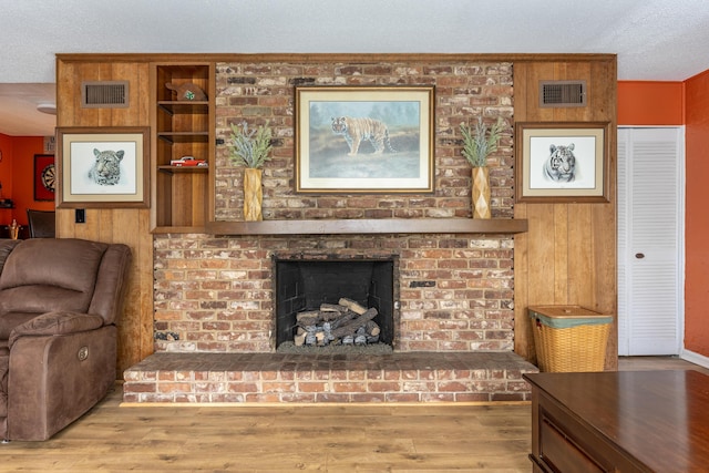 living room with wood walls, a textured ceiling, a fireplace, and light hardwood / wood-style flooring