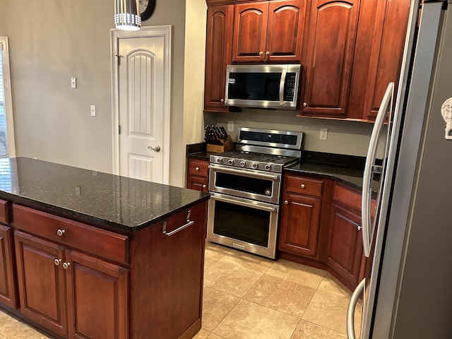 kitchen with appliances with stainless steel finishes, decorative light fixtures, light tile patterned floors, and dark stone counters