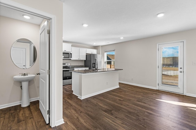 kitchen with dark wood-type flooring, an island with sink, white cabinets, appliances with stainless steel finishes, and sink