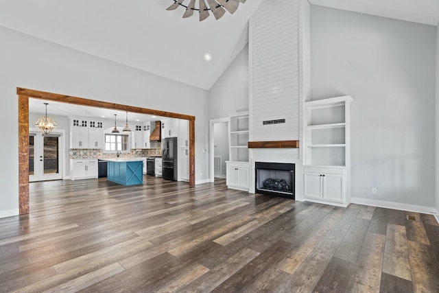 unfurnished living room featuring dark hardwood / wood-style floors, a large fireplace, high vaulted ceiling, and a chandelier