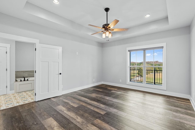 unfurnished room featuring a raised ceiling, ceiling fan, and dark wood-type flooring