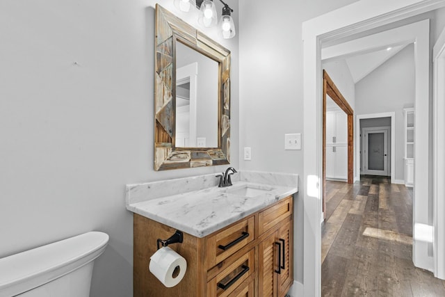 bathroom with hardwood / wood-style flooring, vanity, toilet, and lofted ceiling