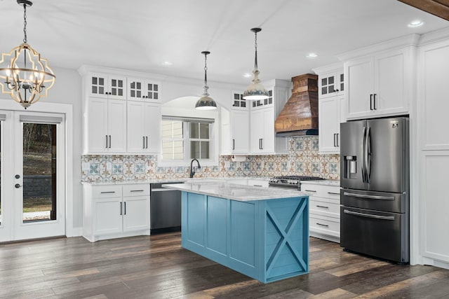 kitchen with white cabinets, custom exhaust hood, hanging light fixtures, and appliances with stainless steel finishes