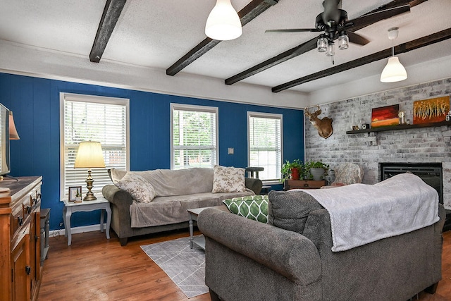 living room with dark wood-type flooring, ceiling fan, a textured ceiling, a fireplace, and beam ceiling