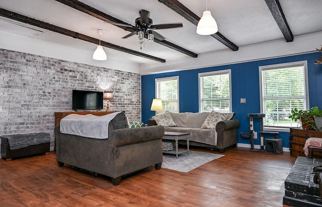 living room with beamed ceiling, ceiling fan, dark wood-type flooring, and brick wall