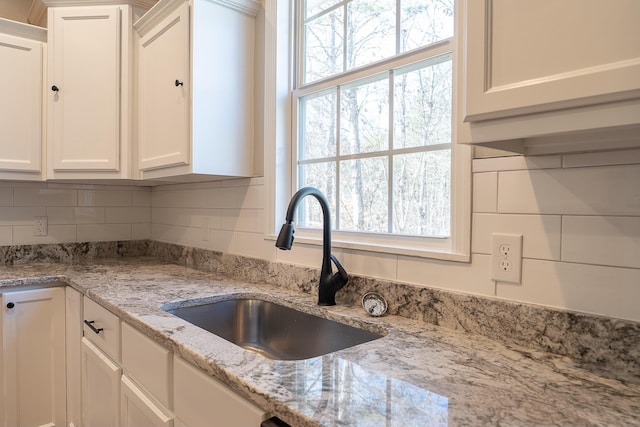 kitchen with light stone countertops, sink, and white cabinetry