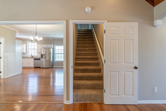 stairs featuring wood-type flooring, ornamental molding, and a notable chandelier