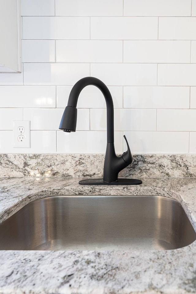 interior details with light stone counters, sink, and white cabinets