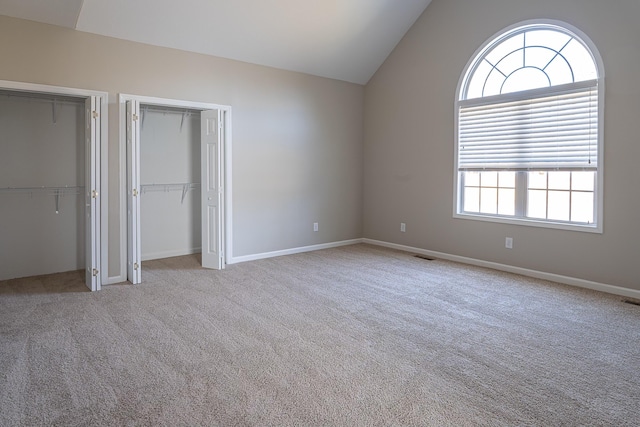 unfurnished bedroom featuring lofted ceiling, two closets, and light carpet